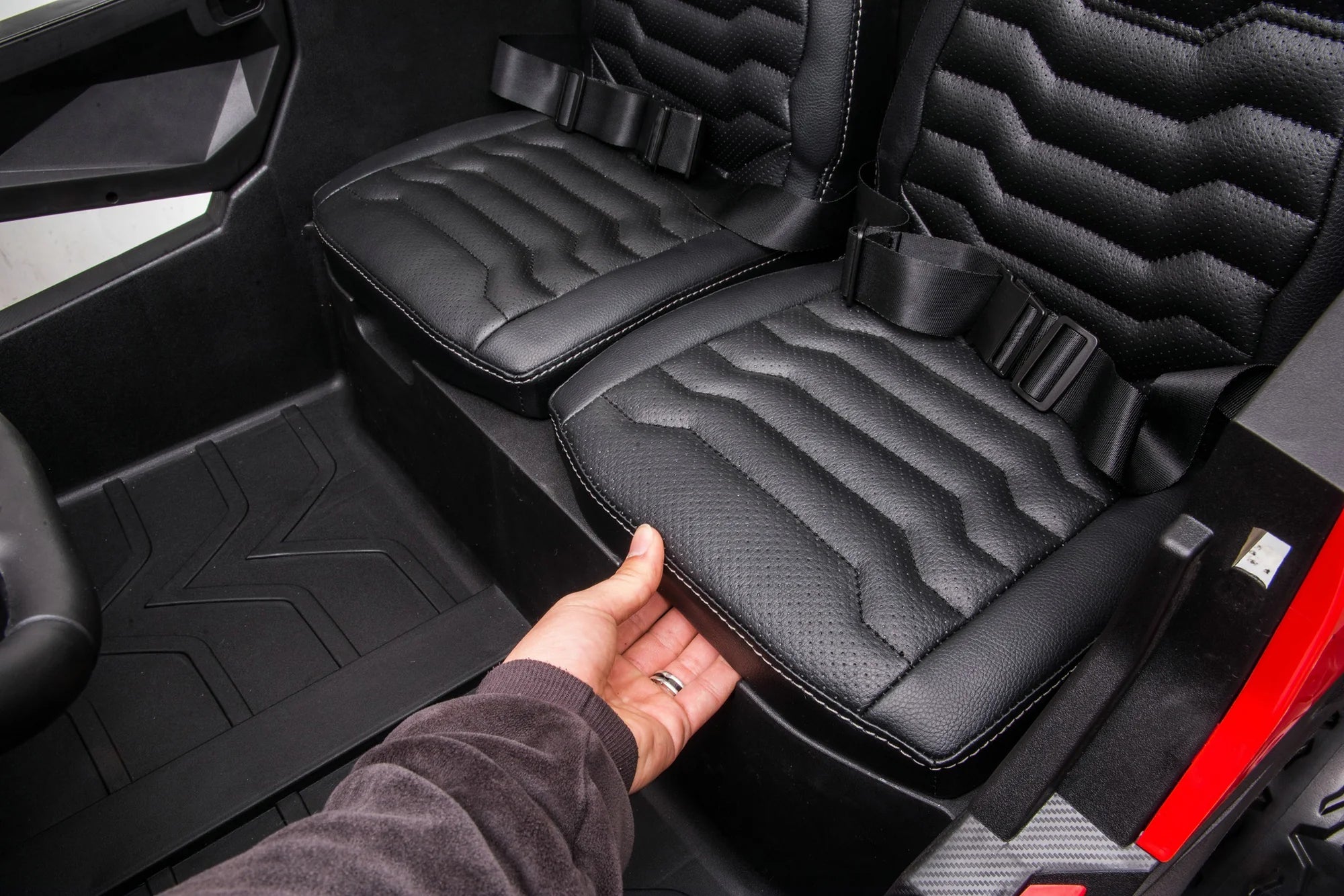 Hand lifting padded black leather seat of the two-seater Stinger Buggy XL 24V kids ride-on car interior.