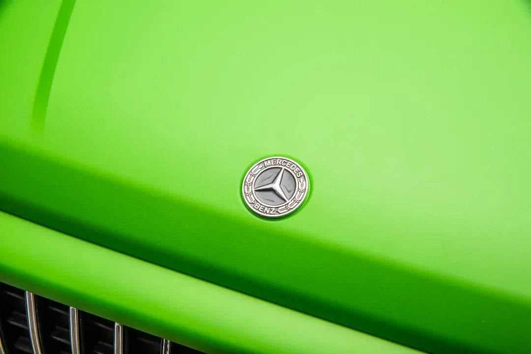 Close-up of Mercedes-Benz silver logo badge on green hood of licensed 24V 14Ah kids ride-on AMG G63 car