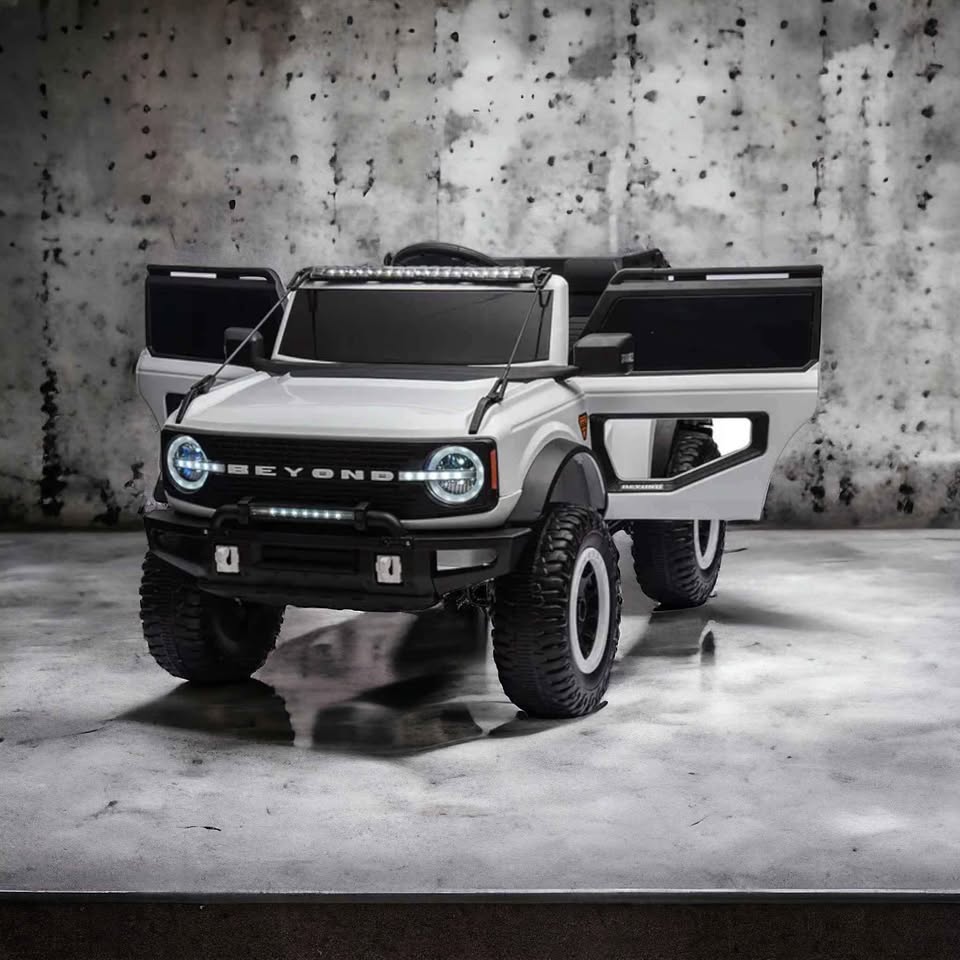 White Ride-On Jeep Beyond 12V 4WD SUV for kids with open doors, headlights on, and rugged tires on concrete floor