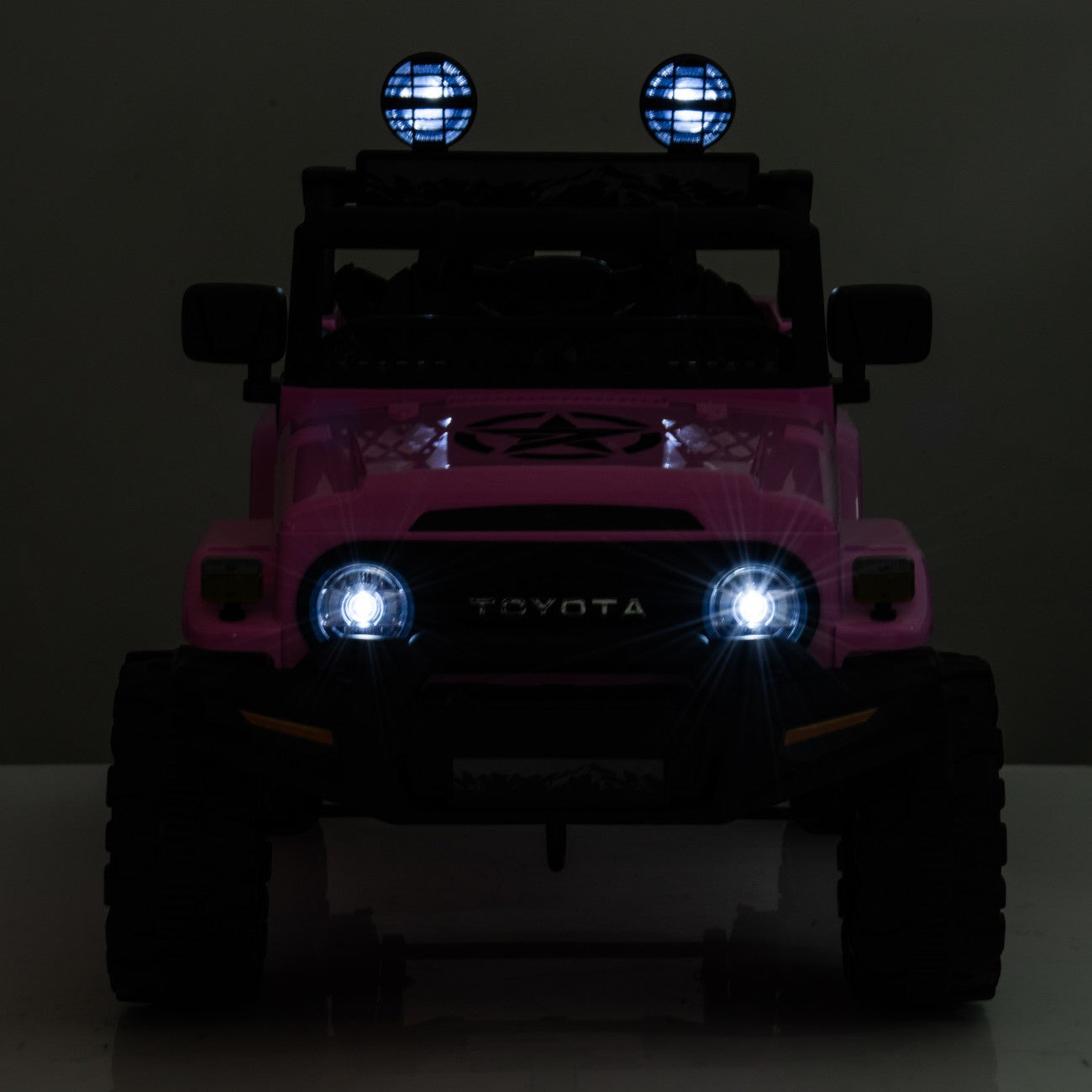 Front view of pink Toyota FJ Cruiser licensed electric toy car with headlights and roof spotlights on at night.