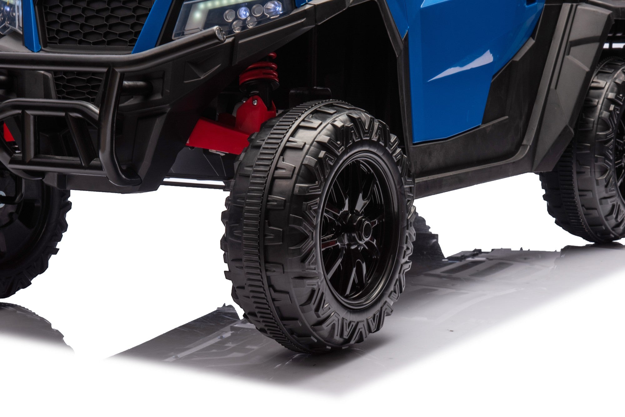 Close-up of front wheel and suspension of blue 24V ride-on electric dump truck with rugged tires and black rim.