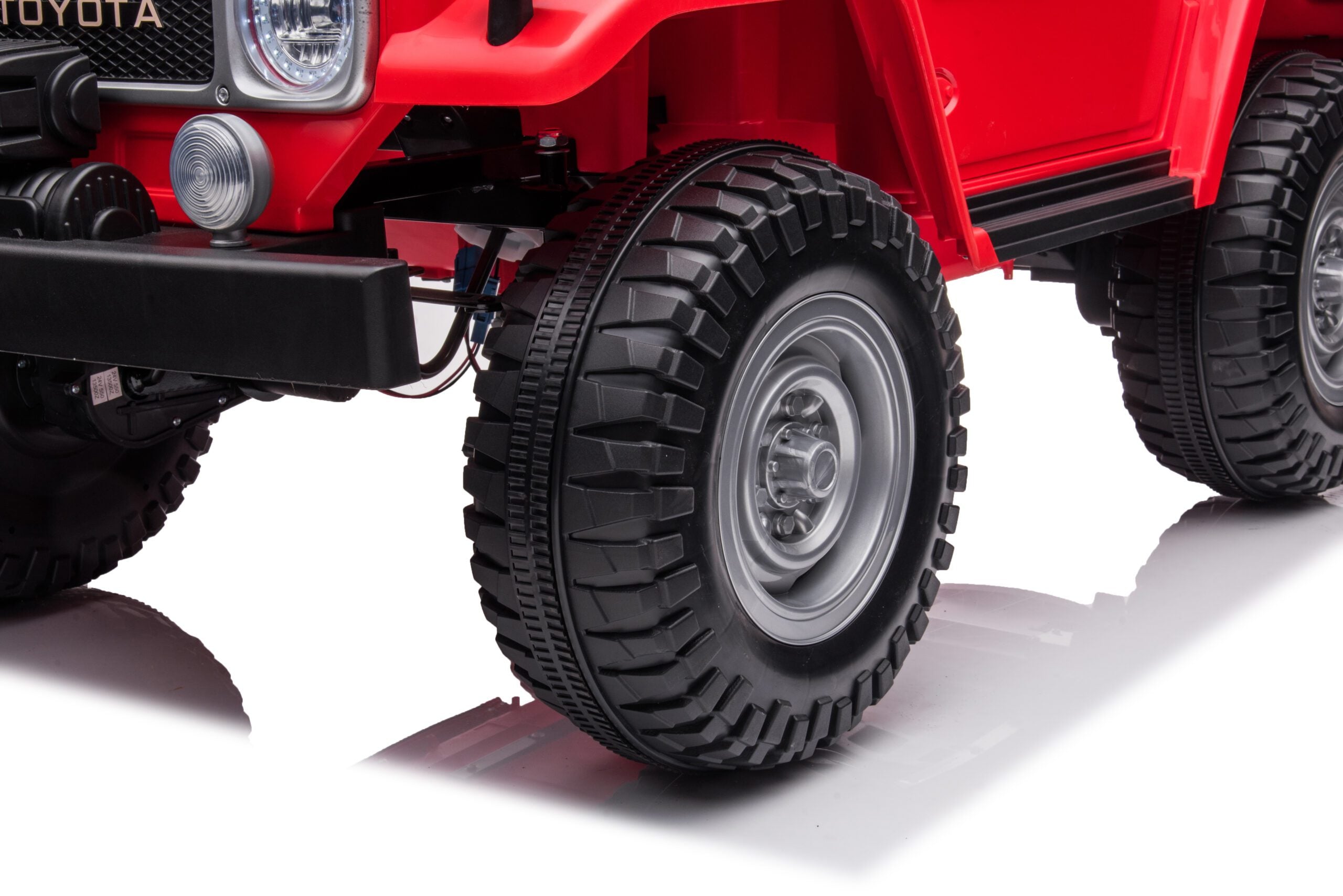 Close-up of front tire and suspension on red 24V 4WD Toyota FJ-40 kids ride-on electric SUV toy car