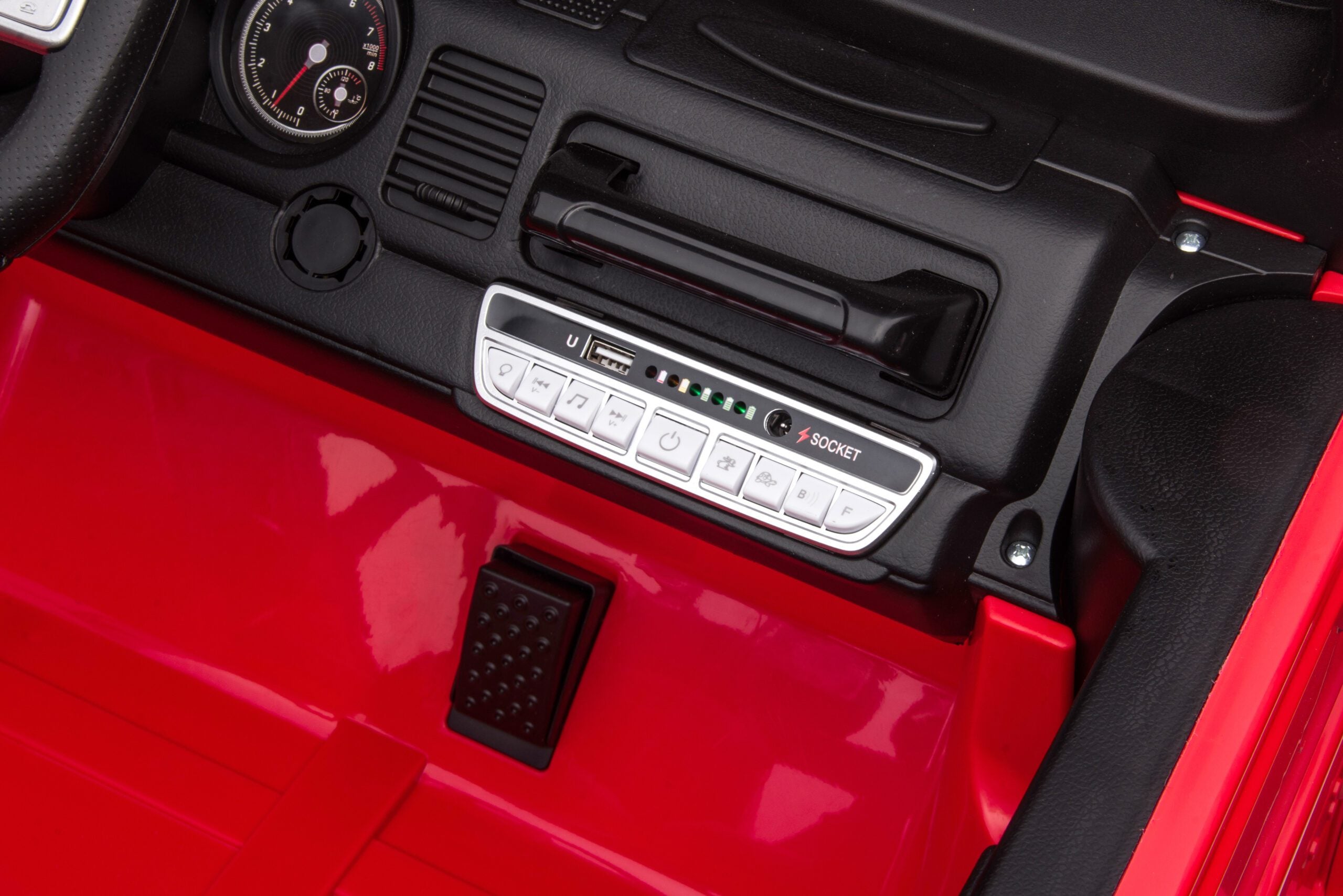 Close-up of red Toyota FJ-40 kids ride-on car dashboard and foot pedal with audio control panel.