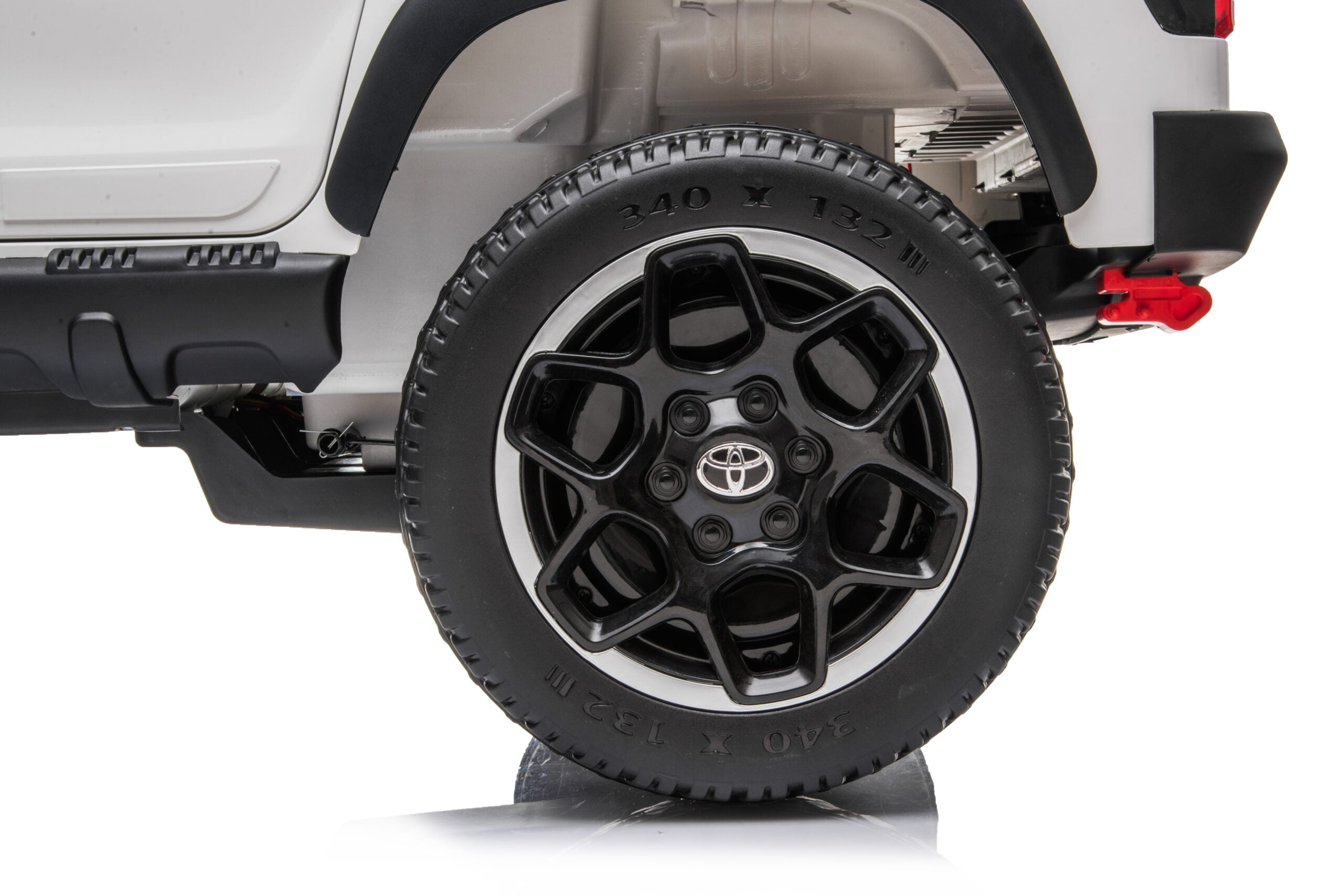 Close-up of black Toyota Hilux ride-on car wheel with realistic tire tread and white body details visible above.