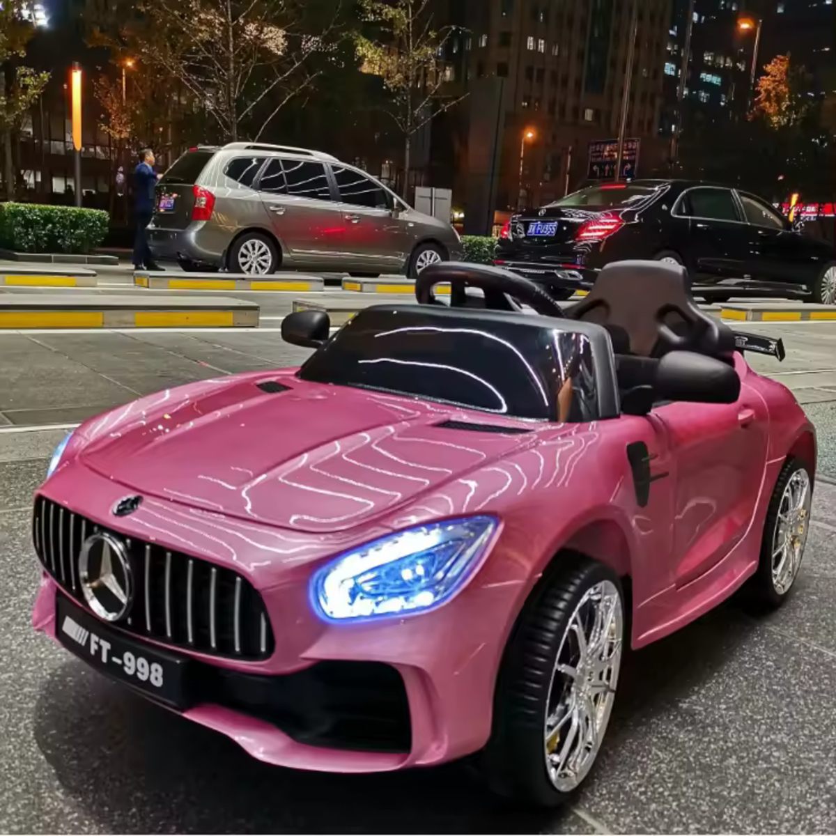 Pink 12V Mercedes-Benz AMG GTR kids electric ride-on car with LED lights and realistic details parked at night.