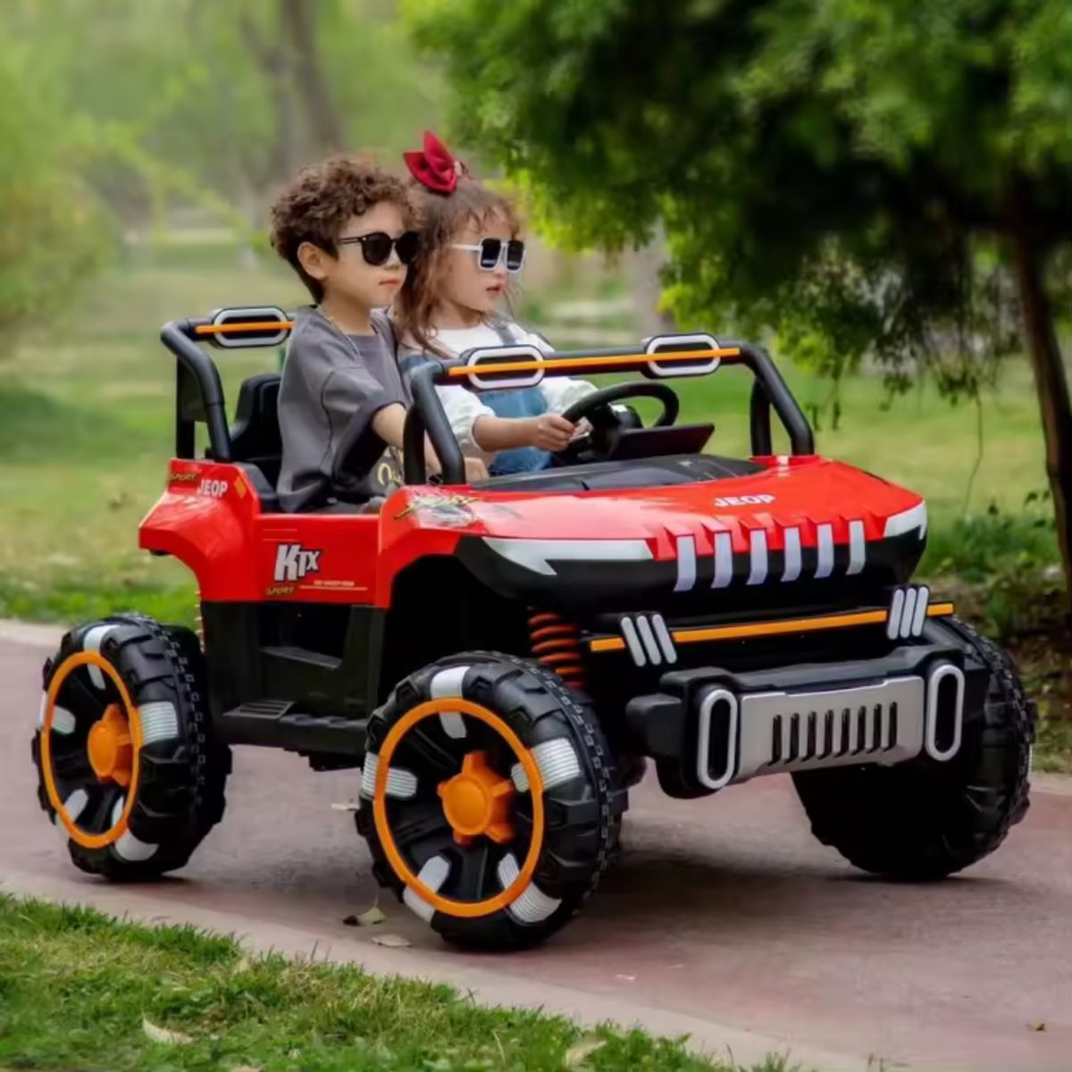 Two kids wearing sunglasses riding a red 24V 2-seater UTV ride-on buggy on a paved path outdoors