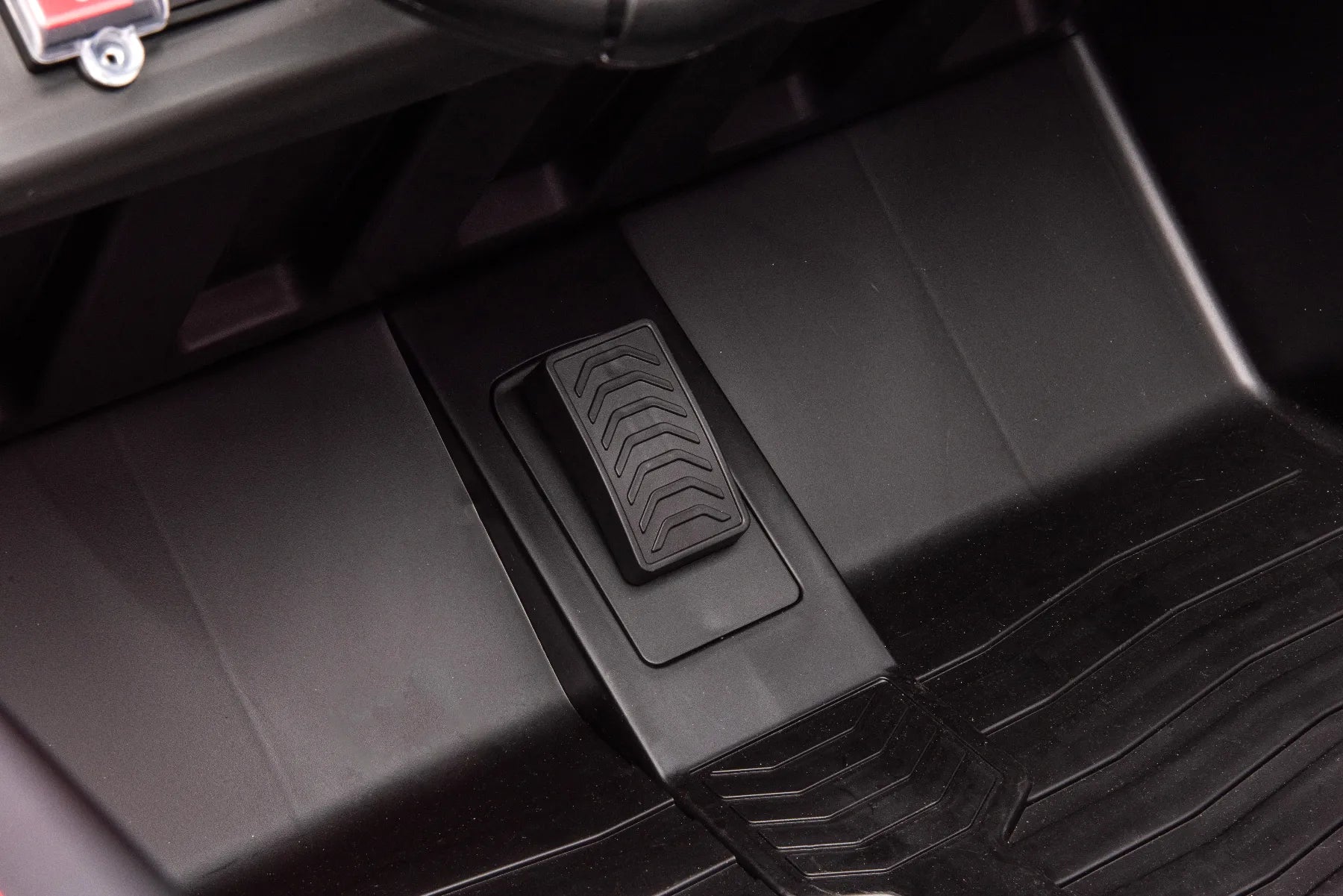 Close-up of black plastic accelerator pedal and textured floor mat inside red 24V two-seater kids electric ride-on buggy