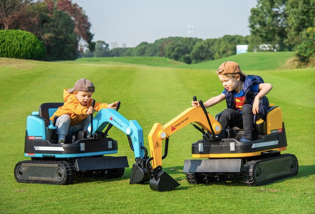 Two young boys playing outdoors on ride-on electric excavator toys with manual digger arms on grass field