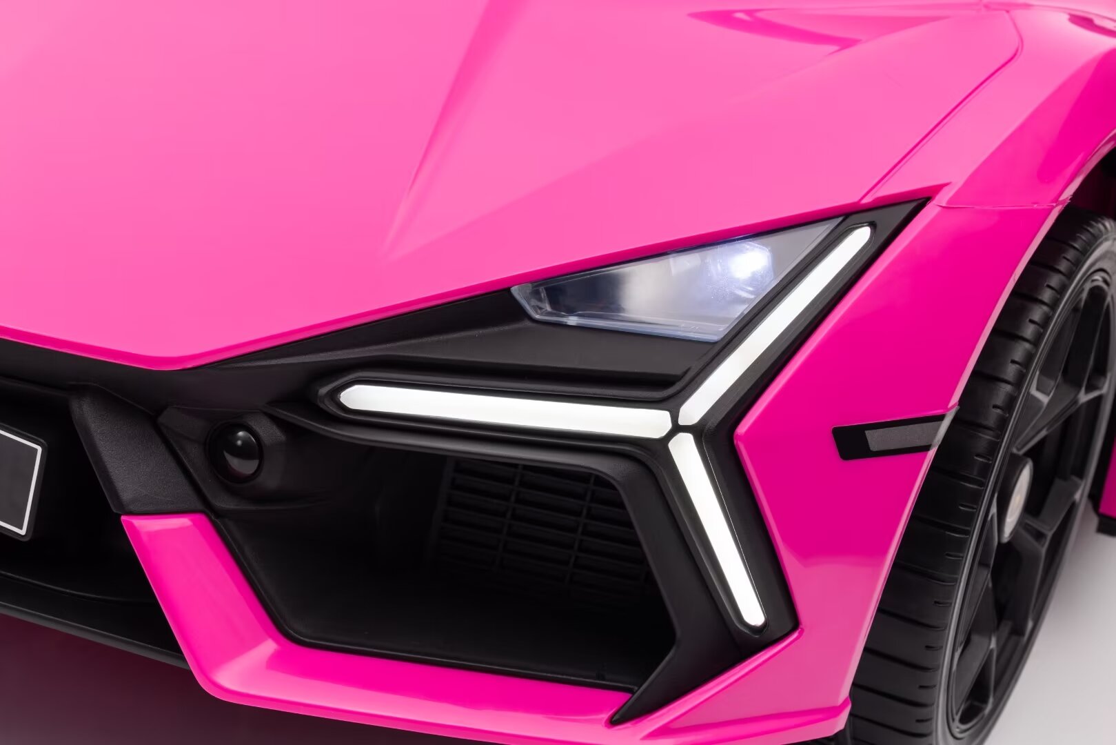 Close-up of pink Lamborghini Revuelto kids electric ride-on car front LED headlight and wheel detail.