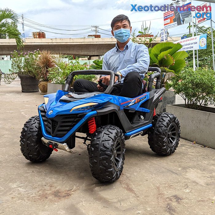 Man wearing mask sitting on blue 2-seater ride on buggy with large soft EVA wheels outdoors