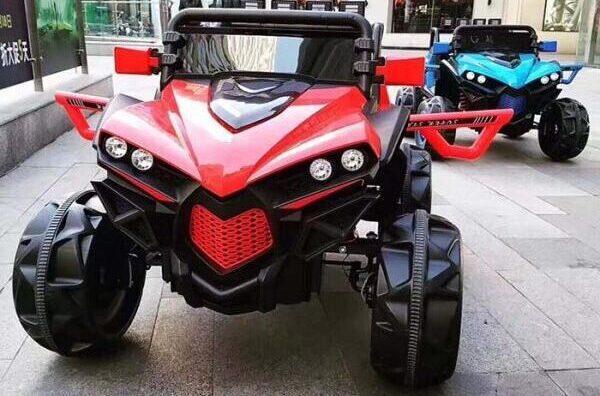 Red and blue 4x4 kids ride-on monster trucks with chunky tires parked on a paved surface.