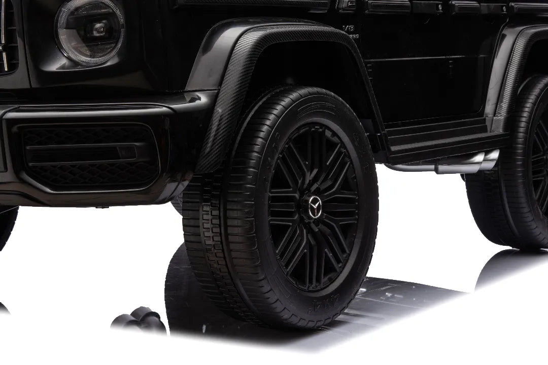 Close-up of black 24V 14Ah licensed Mercedes-AMG G63 kids ride-on car front wheel with branded hubcap and tire tread detail