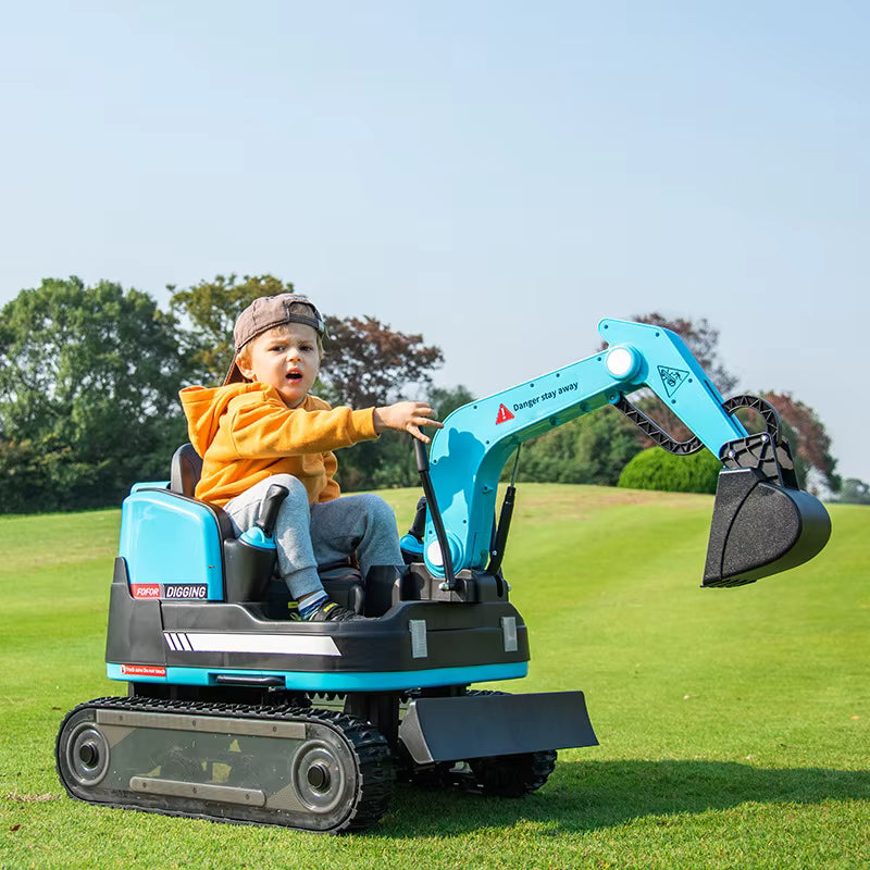 Toddler operating blue 24V ride-on construction digger with manual arm and dual motors on green grass field outdoors