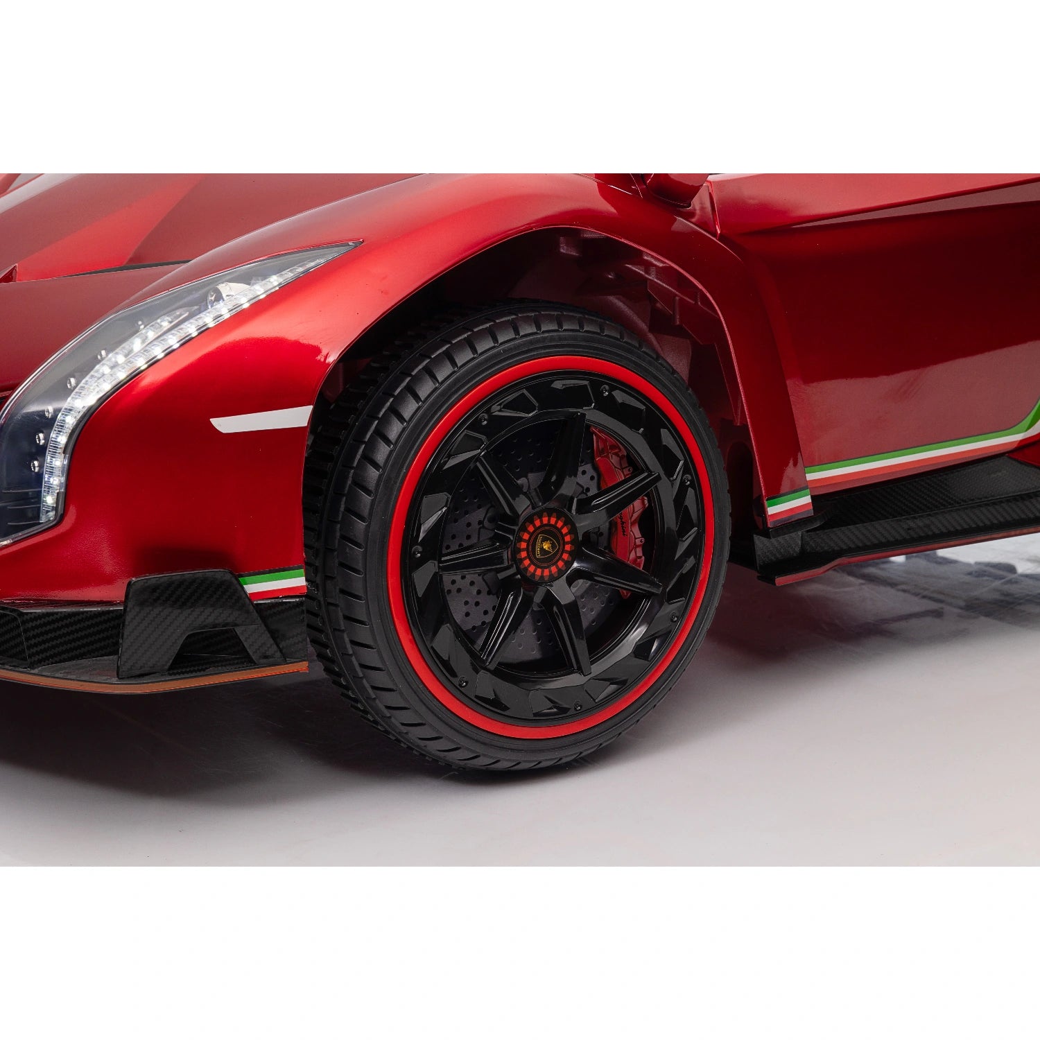 Close-up of red Lamborghini Veneno ride-on car front wheel with black rim and red stripe on tire for kids.