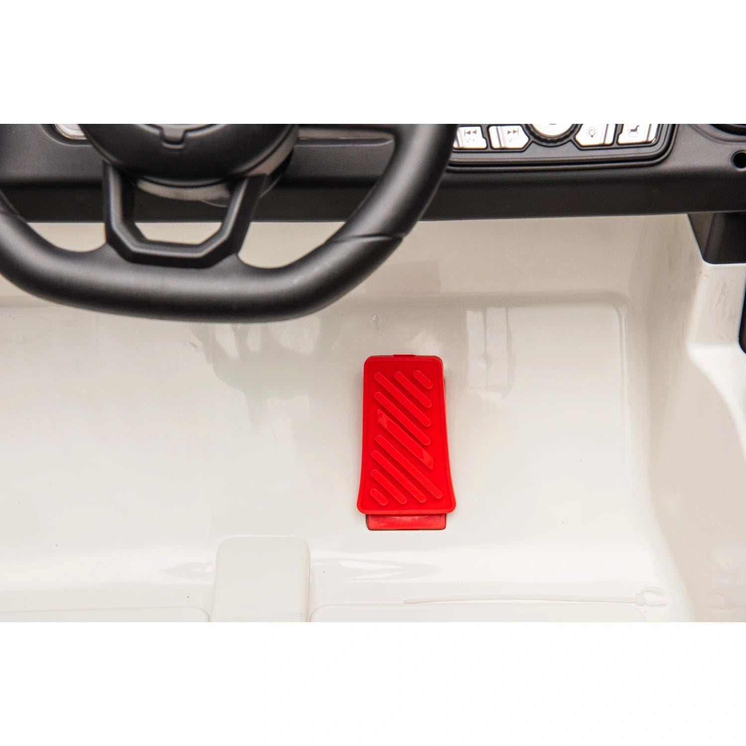 Close-up of red accelerator pedal and black steering wheel inside white 12V ride-on jeep style kids electric car.