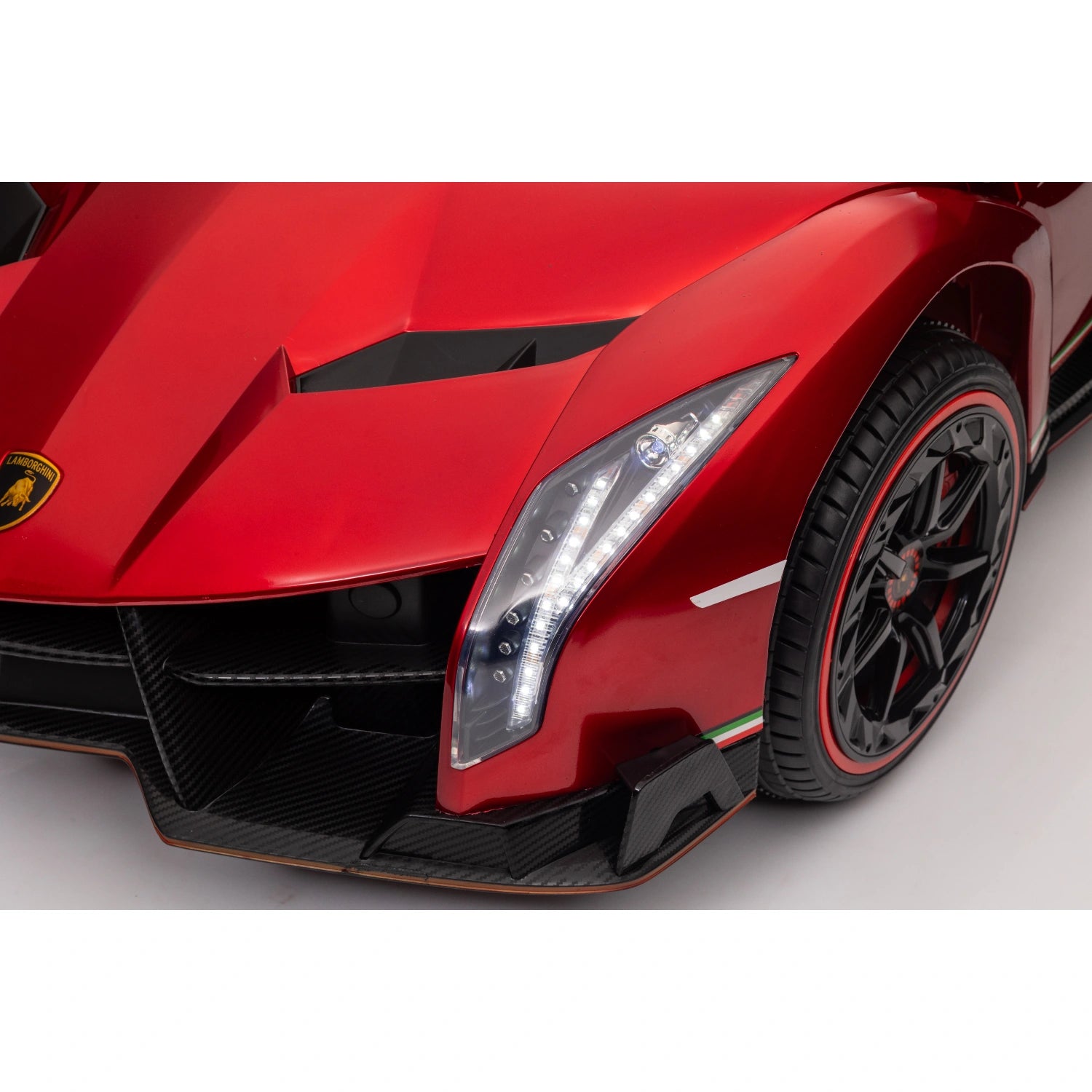 Close-up of red licensed Lamborghini Veneno kids ride-on car front headlight and black wheel with red trim detailing